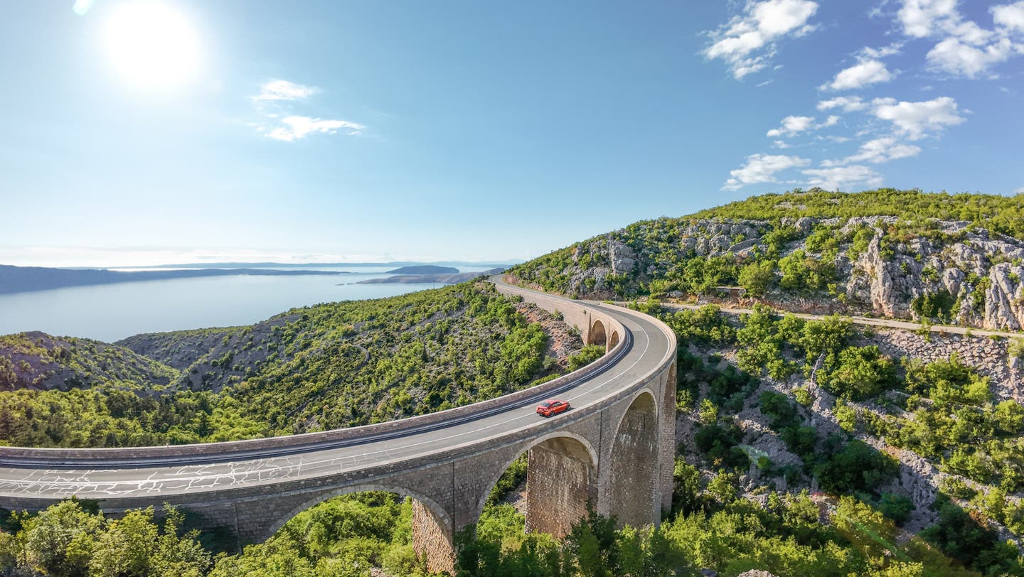 Straße auf Steinviadukt an Mittelmeerküste, ideal für Erlebnisreisen mit dem Auto durch Gebirge und Küstennähe