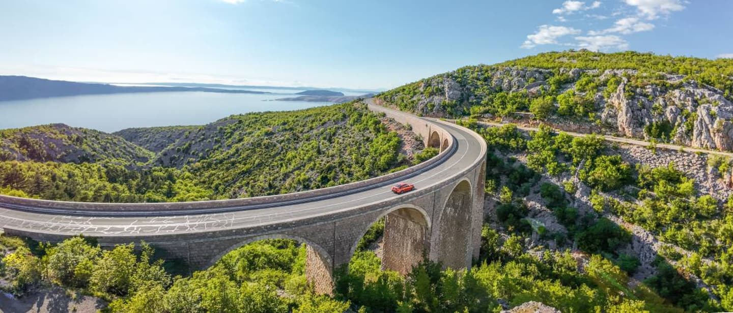 Straße auf Steinviadukt an Mittelmeerküste, ideal für Erlebnisreisen mit dem Auto durch Gebirge und Küstennähe