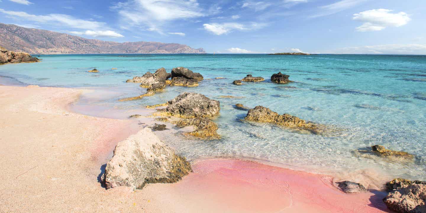 Elafonisi Strand auf Kreta mit rosa Schimmer im Sand, türkisfarbenem Wasser und leuchtendem Morgenhimmel 