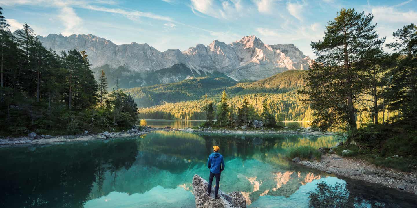 Ein Wanderer steht am Ufer eines Bergsees mit Blick auf die bayerischen Alpen
