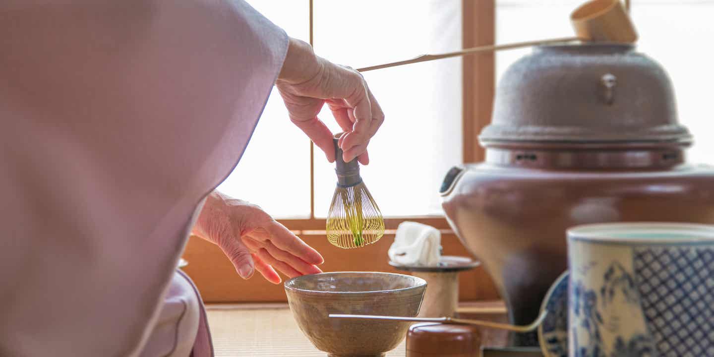 Frau in weißem Gewand bei einer klassischen japanischen Teezeremonie mit Teebesen
