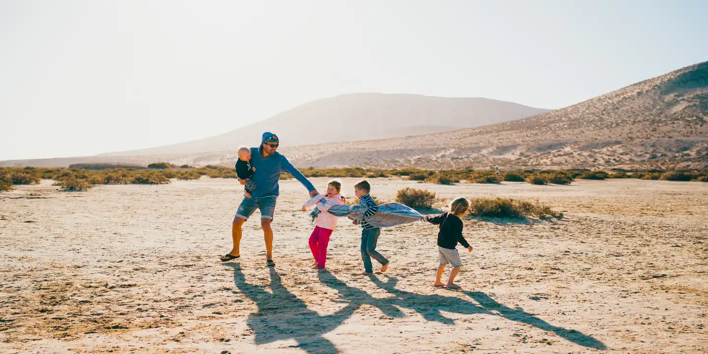 Familie spielt auf einer weiten Sandfläche an der Küste Fuerteventuras vor karger Vulkanlandschaft