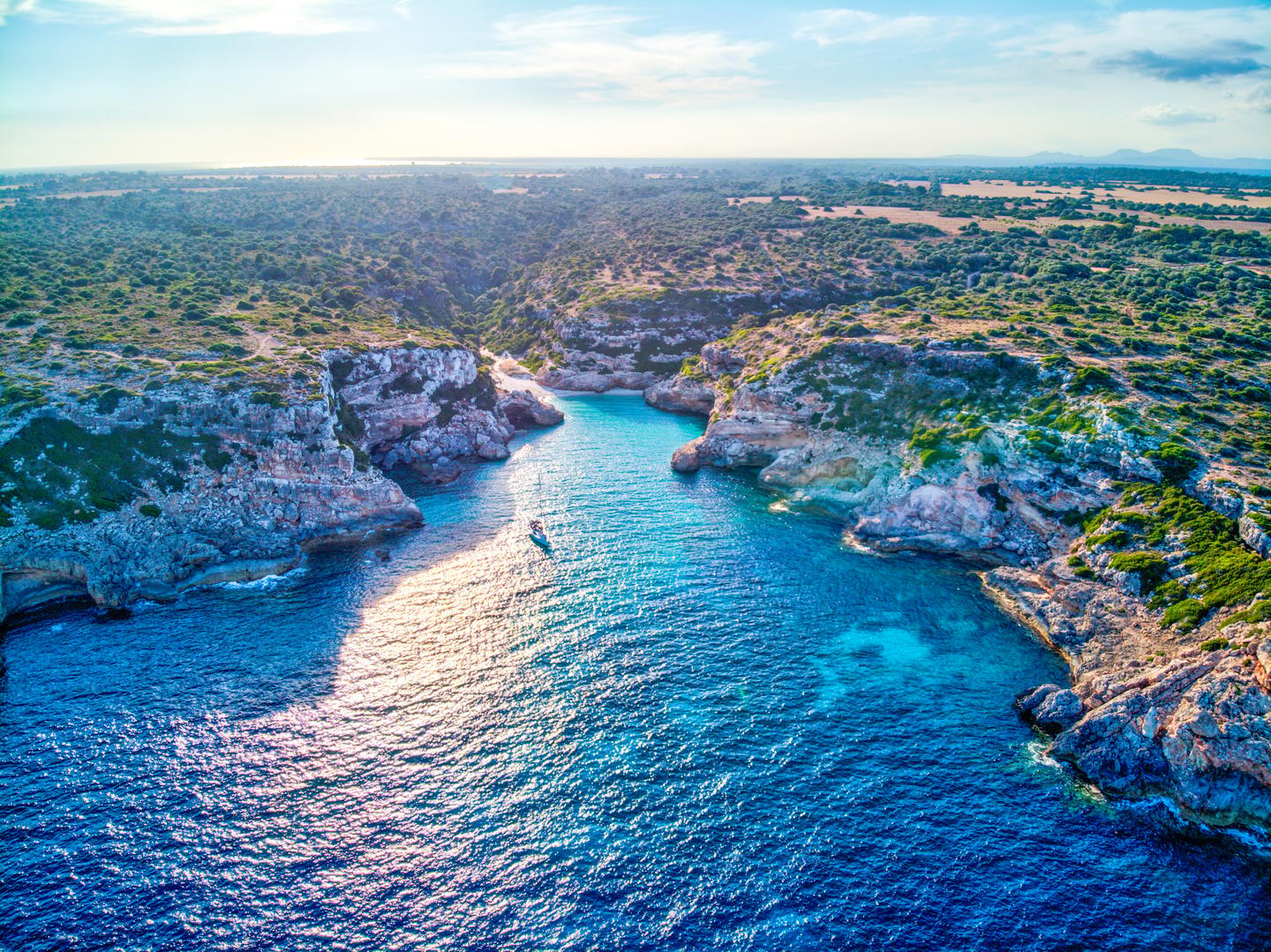 Luftaufnahme der Cala Marmols auf Mallorca mit schmaler Felsbucht, ruhigem Meer und einem einzelnen Boot nahe der Küste
