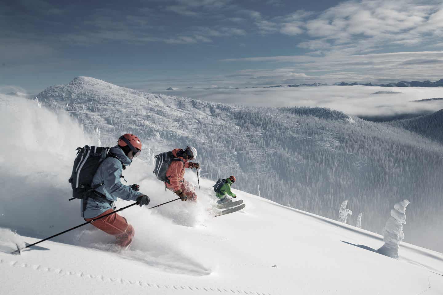 Drei Skifahrer bei der Abfahrt in einem Skigebiet in Kanada auf der Piste an einem strahlend sonnigen Tag.