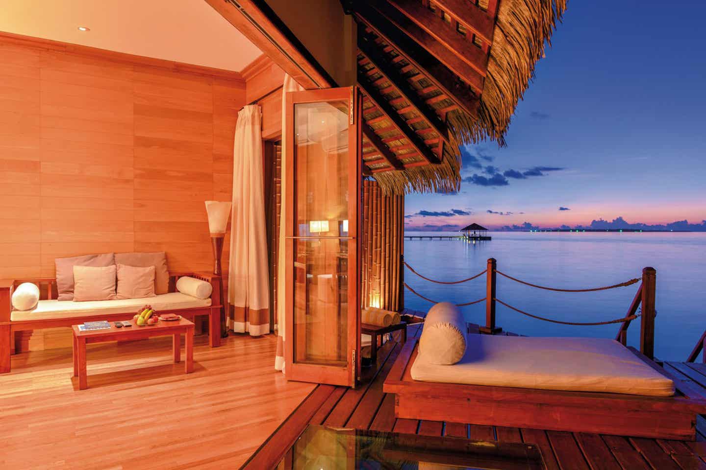 Blick von der Terrasse eines Wasserbungalows aufs Meer bei Sonnenuntergang
