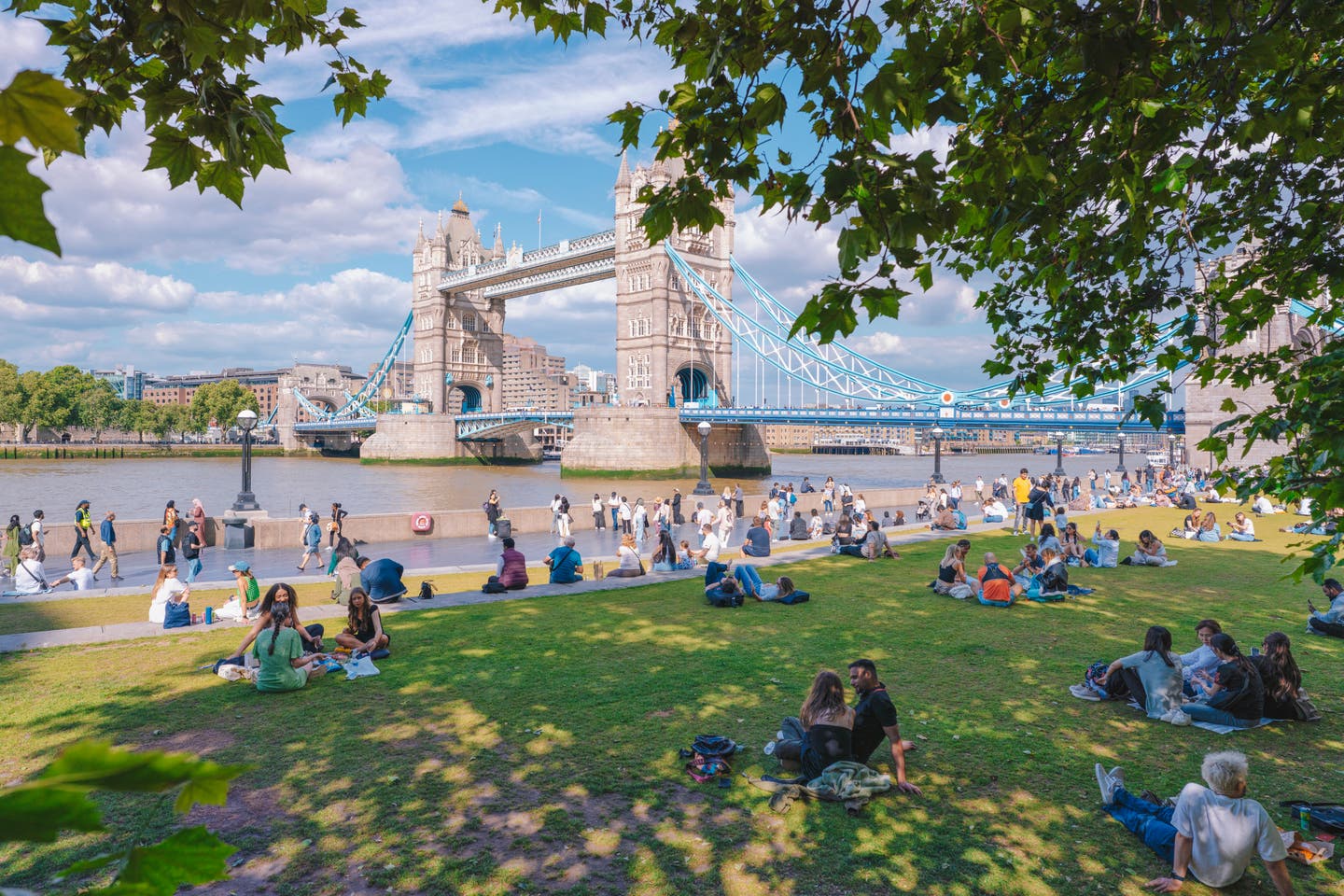 Blick auf die Tower Bridge über die Themse in London, im Vordergrund die Grünfläche Potter's Field auf der Menschen verweilen