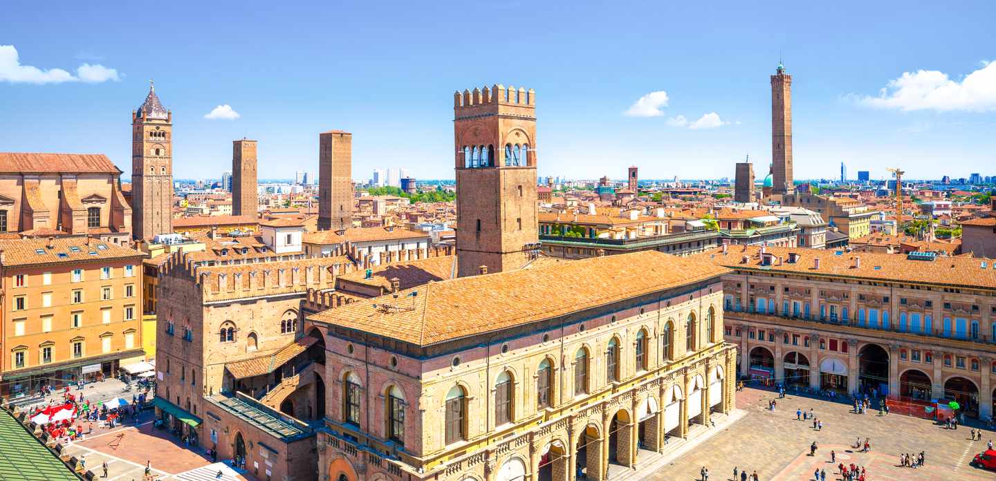 Urlaub in Bologna: Panoramablick mit Arkadengängen, Türmen und der Piazza Maggiore bei klarem Himmel