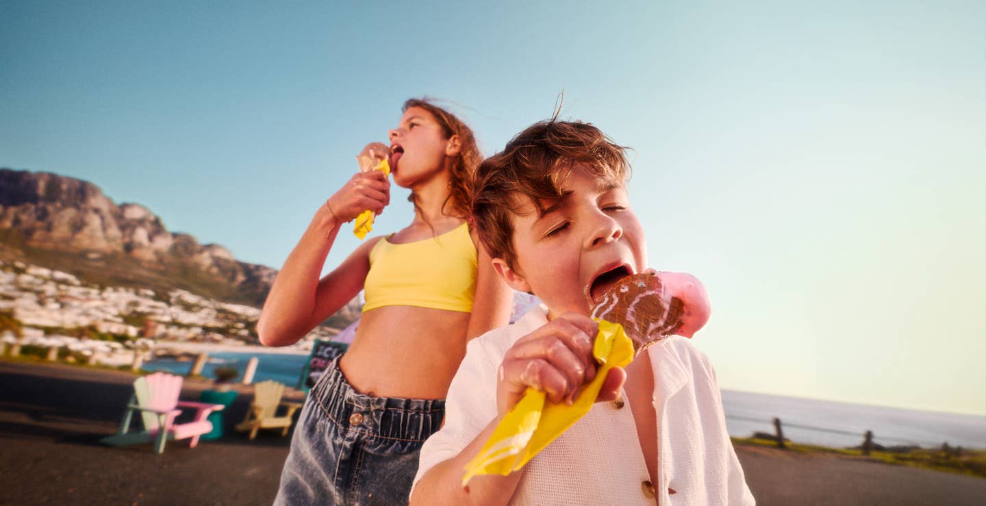 Zwei Kinder essen im Familienurlaub ein Eis am Strand