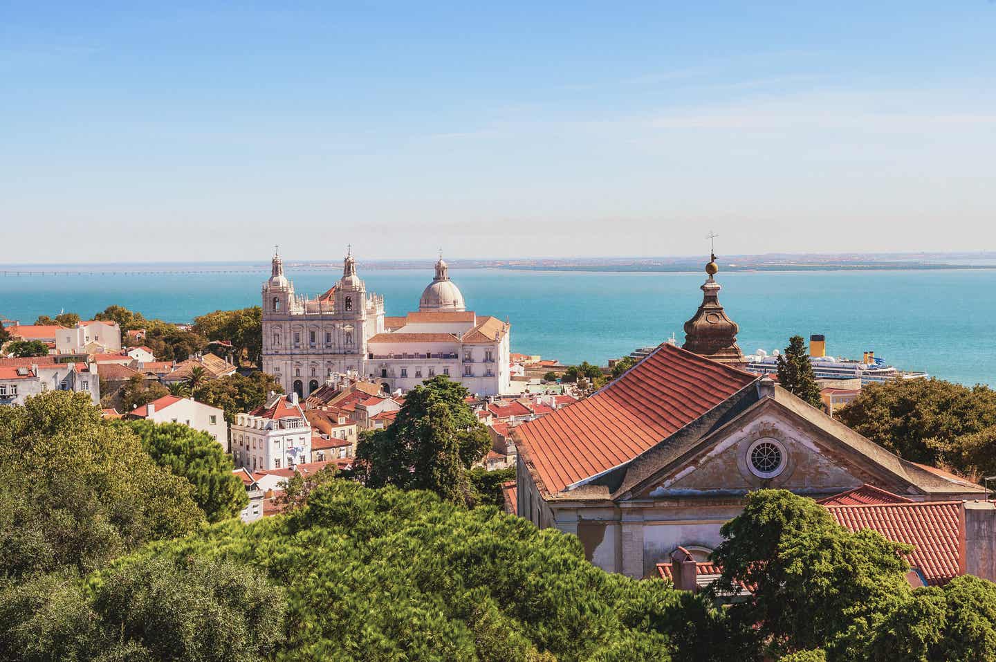 Lissabon als Herbstferien Reiseziel: Panoramablick über die Kathedrale, bunte Häuser und das Meer