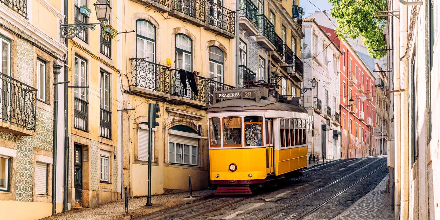 Gelbe Straßenbahn Tram 28E fährt durch enge Gasse im Viertel Alfama in Lissabon