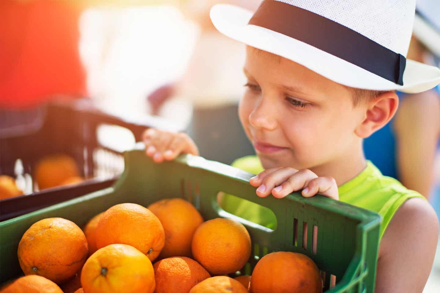 Ein kleiner Junge mit Hut schaut auf eine Kiste mit Orangen