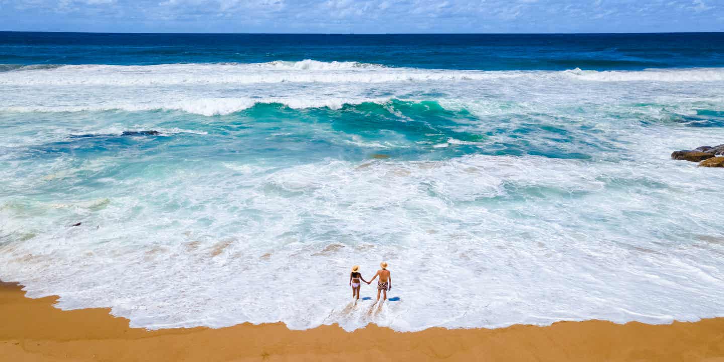 Paar am Strand von Mission Rocks bei Cape Vidal in St. Lucia, Südafrika – mit Wellen, Sand und Felsküste im iSimangaliso Wetland Park