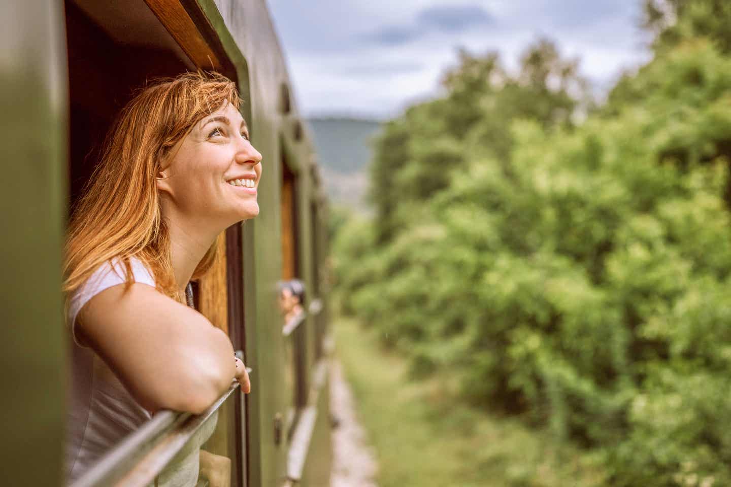 Junge Frau lehnt sich beim Zugfahren aus dem Fenster und wirkt wie in einer Filmszene – Main Character Energy beim Reisen