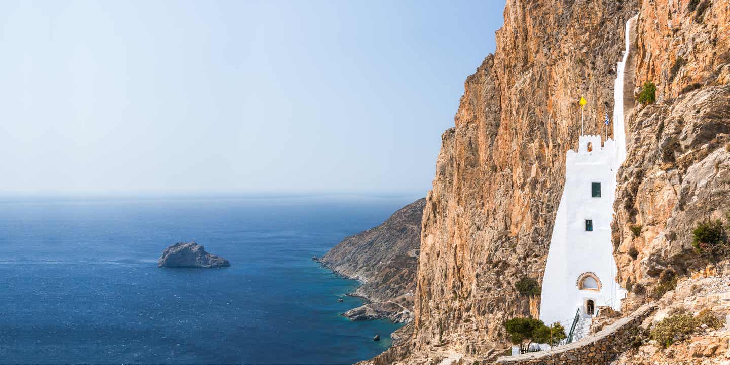 Beeindruckender Drehort in Griechenland: Weißes Gebäude mitten im Fels, darunter das Meer