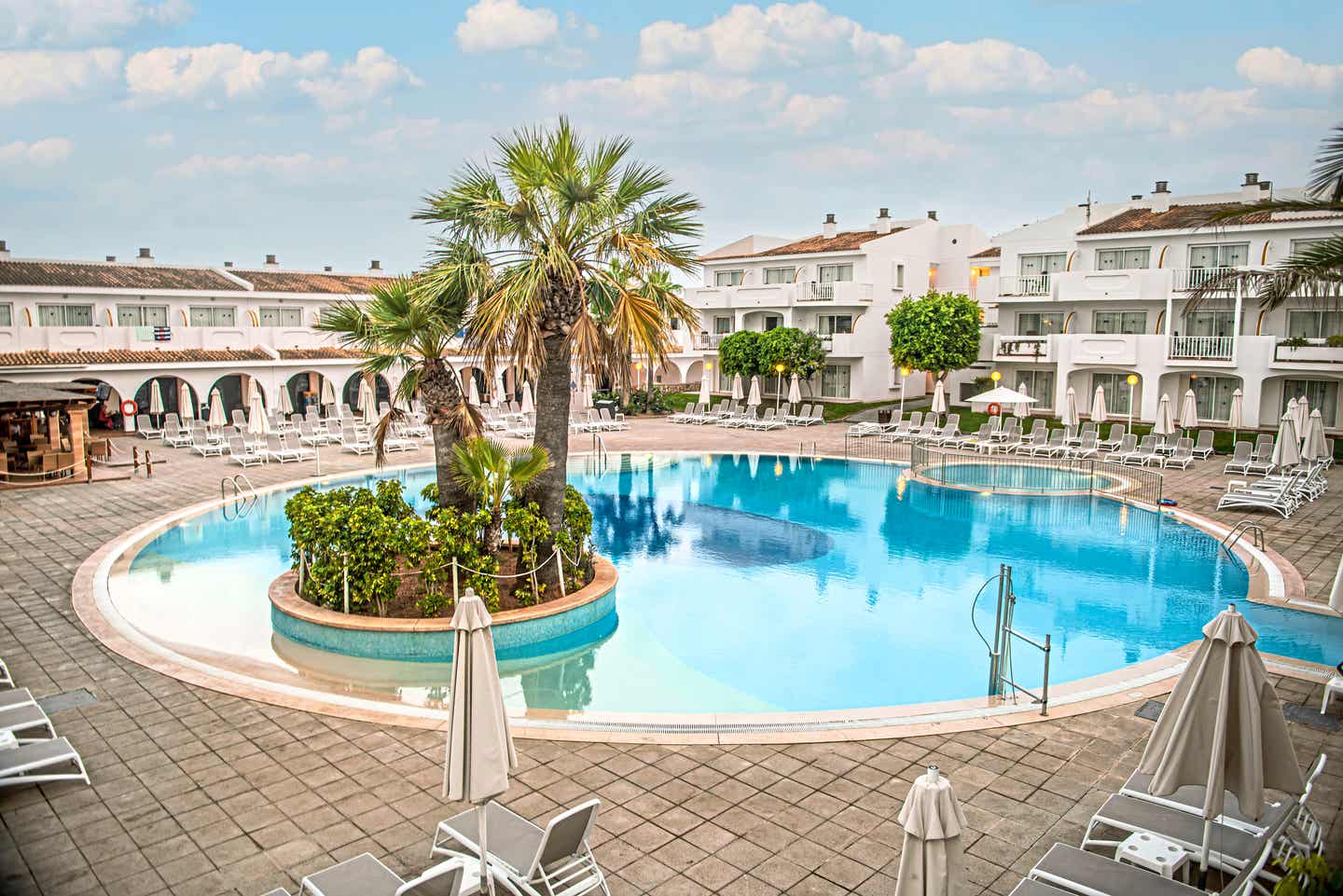 Eines der besten Familienhotels auf Mallorca das Blau Punta Reina Resort auf Mallorca – Poolbereich mit Palmen, Sonnenliegen und umgeben von weißen Gebäuden