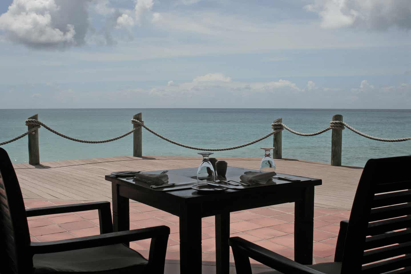 Antigua Urlaub mit DERTOUR. Tisch für zwei auf einer Terrasse am Meer vor Antigua