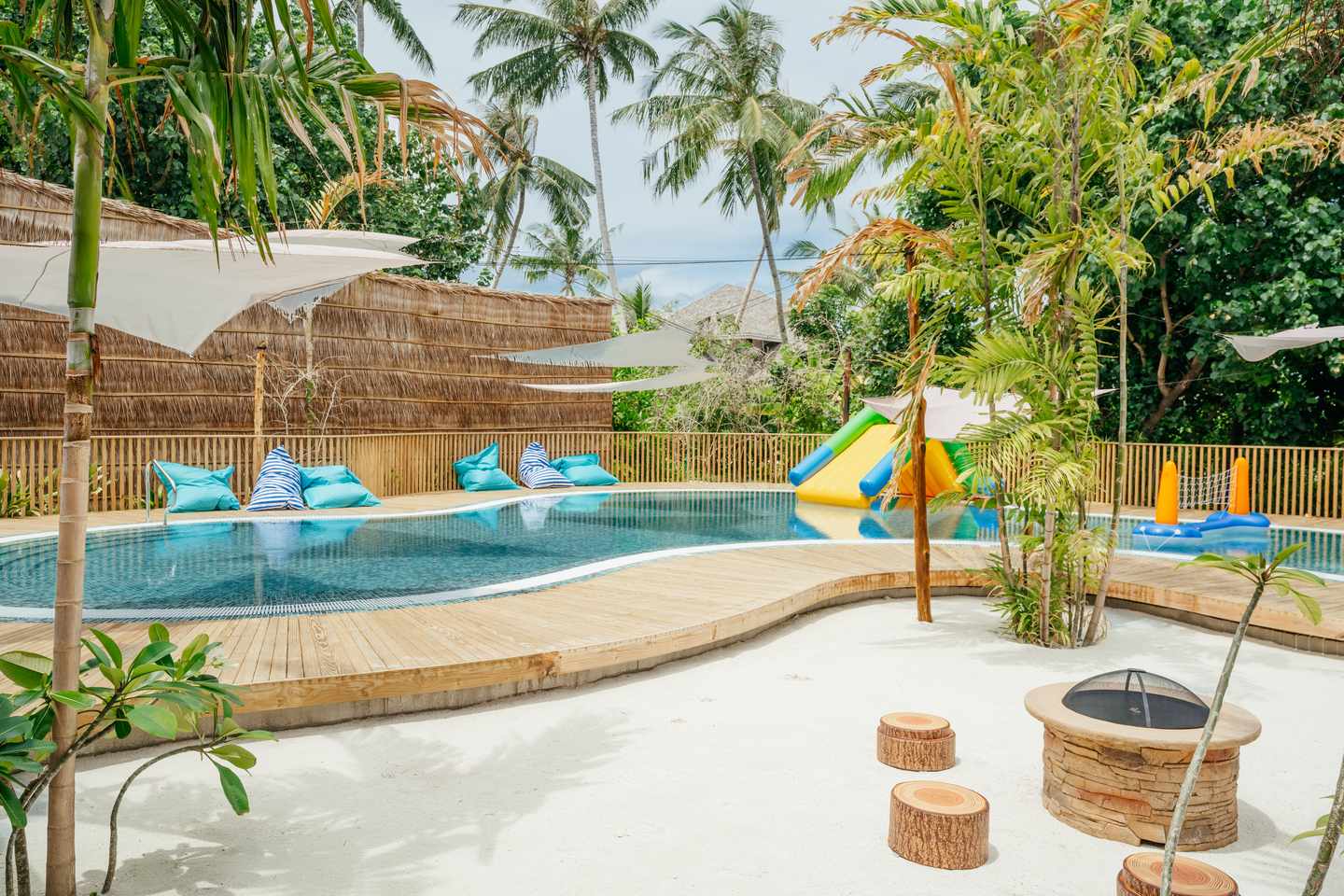 Kinderpool mit kleiner Rutsche und Liegekissen am Rand, umgeben von Palmen und tropischen Pflanzen