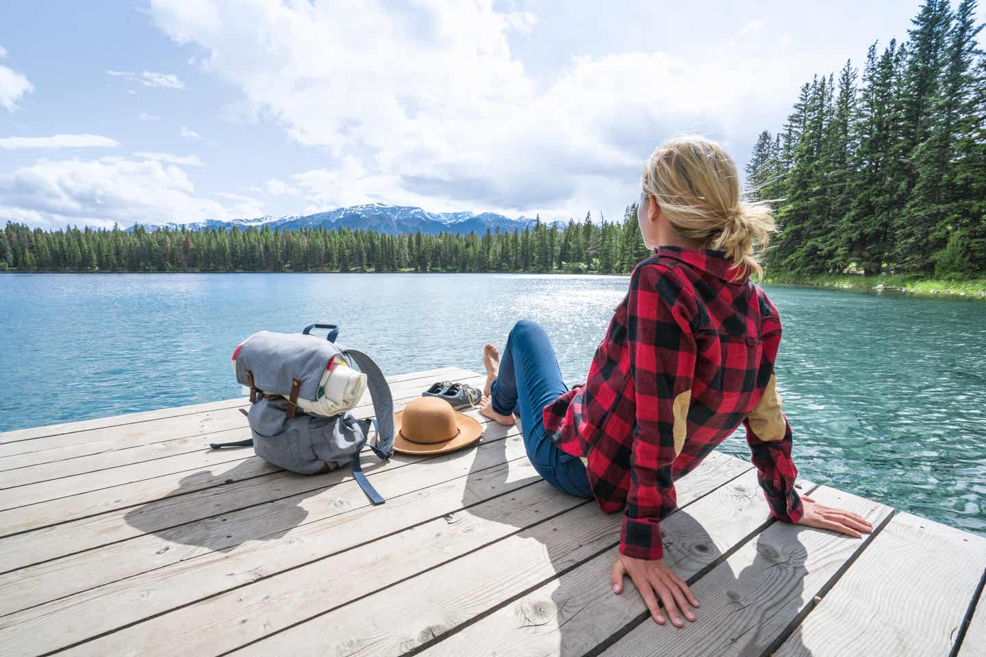 Frau sitzt entspannt auf einem Holzsteg am See in Kanada mit Blick auf Wasser, Berge und Wald im Sommer