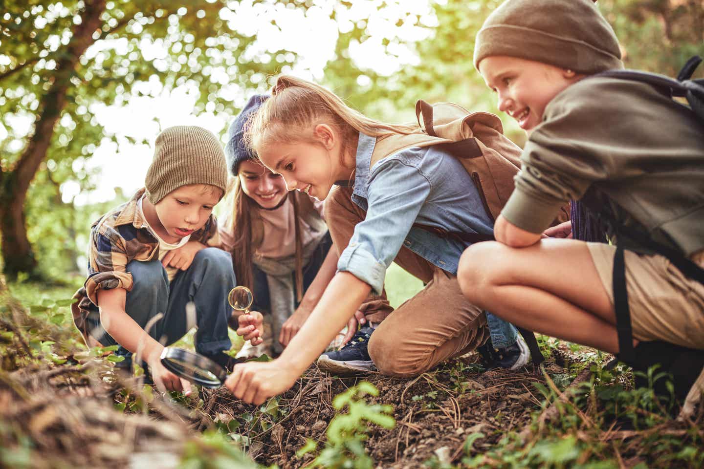 Kinder erkunden spielerisch die Natur im Wald und untersuchen Pflanzen mit Lupe bei einer Outdoor-Aktivität