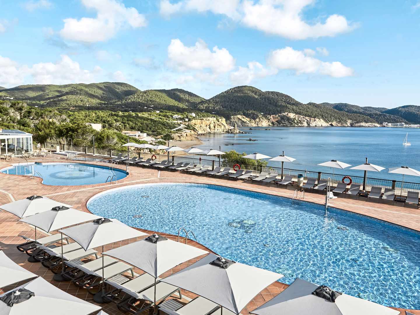 Poolbereich im Sentido Cala Verde auf Ibiza mit Sonnenschirmen, Liegen und weiter Aussicht über die Bucht und das Mittelmeer