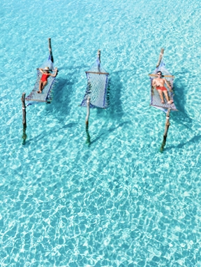 Frühbucherangebote 2026: Luftaufnahme von Personen in roter Badekleidung auf Hängematten im Wasser