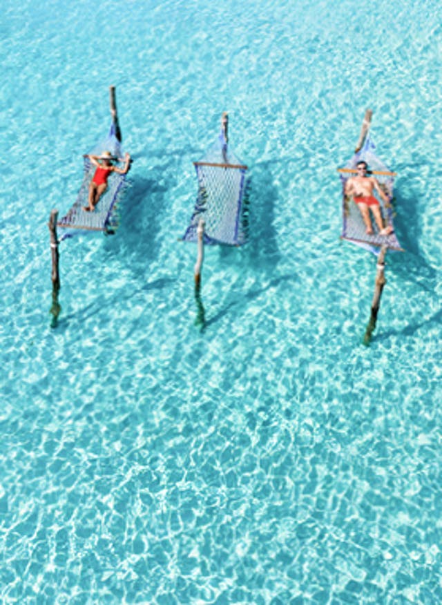 Mehr Infos hier Frühbucherangebote 2026: Luftaufnahme von Personen in roter Badekleidung auf Hängematten im Wasser