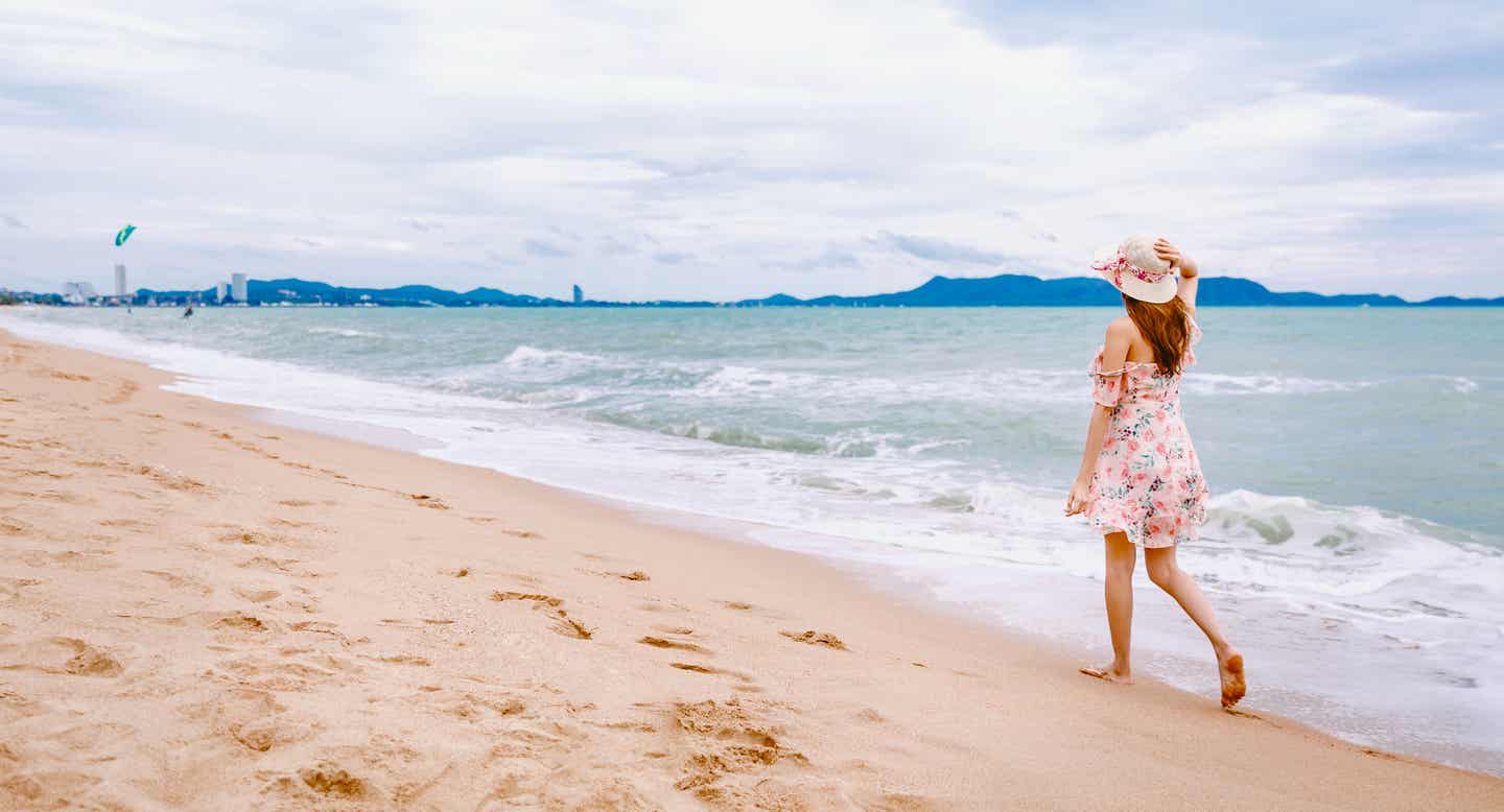 Blick übers Wasser am Wong Amat Beach; eine Frau geht im Sand spazieren