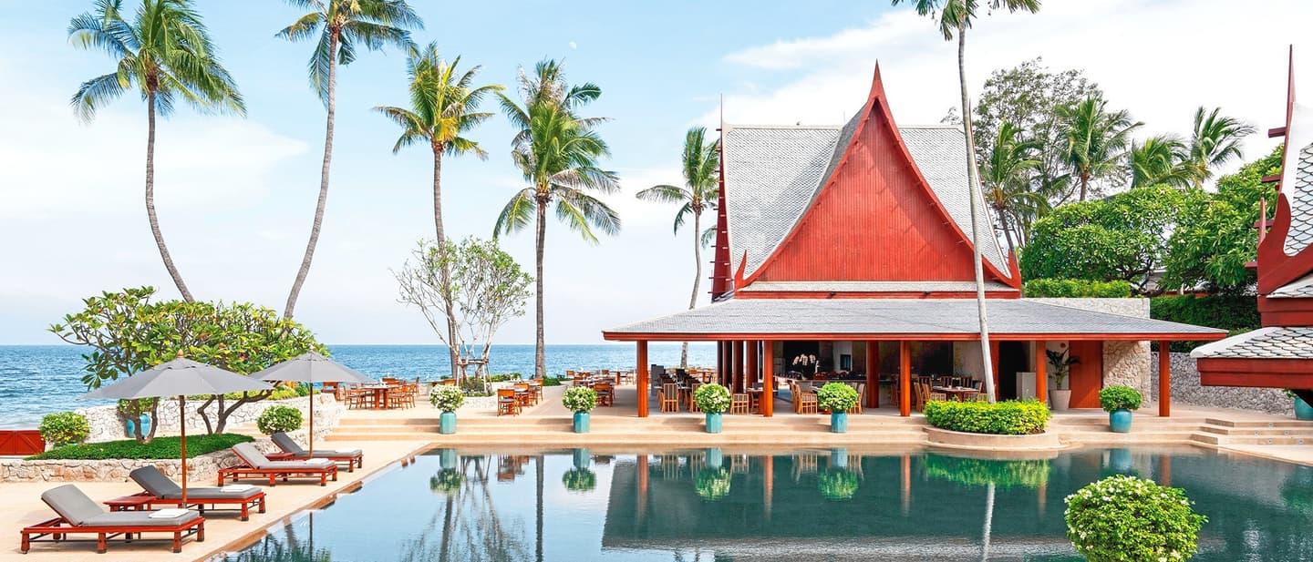 Asiatisches Gebäude mit rotem Holz mit Pool, Liegen, Palmen und Meer im Hintergrund