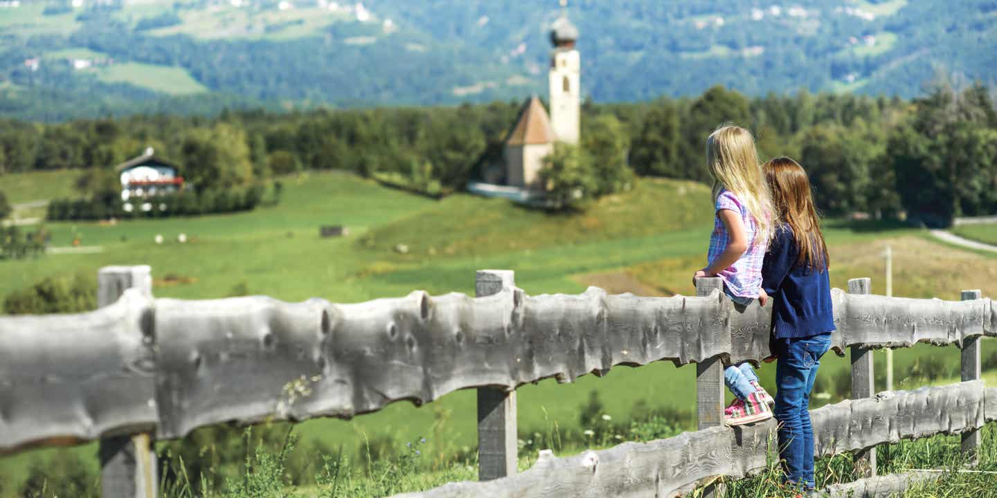Zwei Kinder stehen an einem Holzzaun und blicken auf eine Landschaft in Südtirol