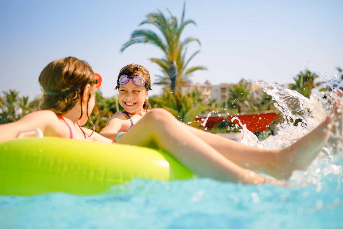 Zwei Kinder lachen im Pool auf einer Luftmatratze, Wasserspaß unter Palmen in einem türkischen Familienhotel 