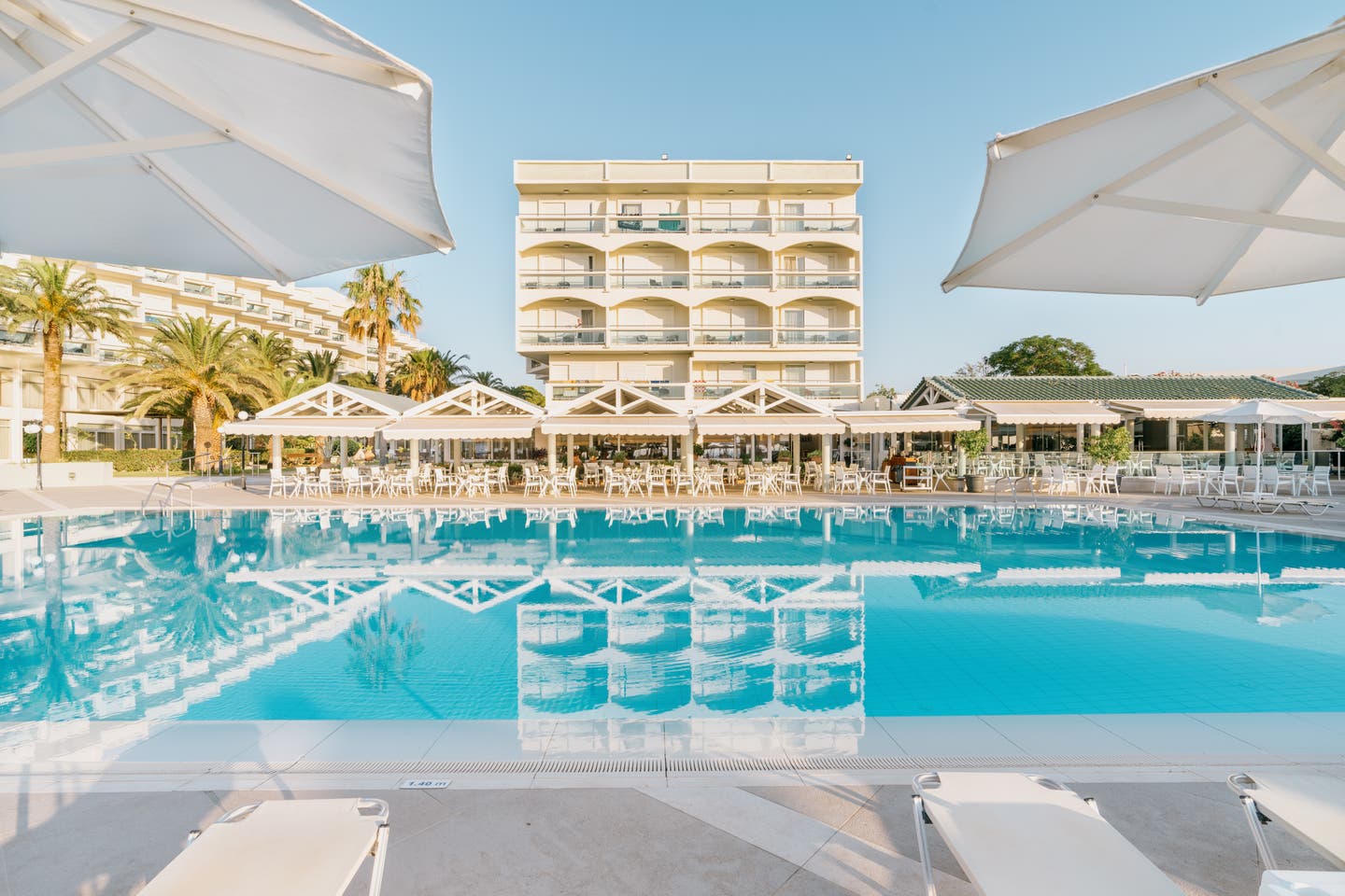 Pool des Apollo Beach mit Sonnenliegen und Hotel im Hintergrund