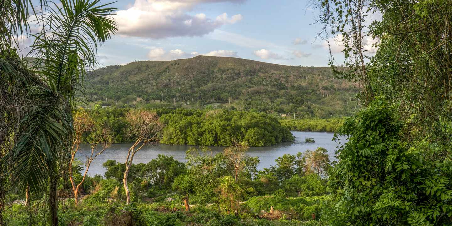 Mantanzas Fluss mit grüner Ufervegetation und Hügel im Yumuri-Tal unter bewölktem Himmel