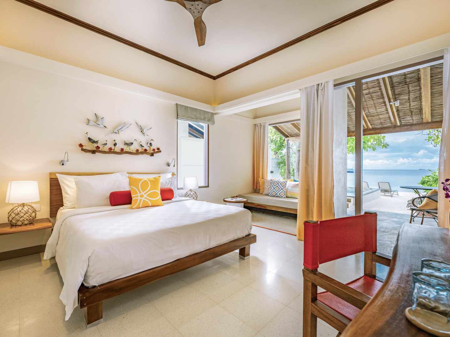 Wohnbereich einer Overwater-Villa im Sentido OBLU auf den Malediven mit Doppelbett, Sitzmöbeln, Terrasse und Blick auf die Lagune