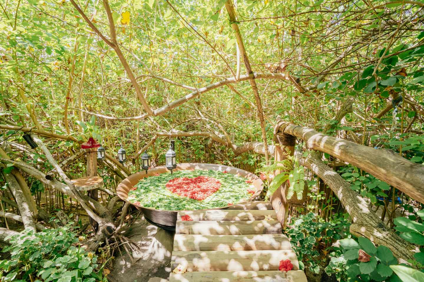 Runde Badewanne mit grünen und roten Blütenblättern bedeckt, die ein Herz formen, inmitten einer wilden Gartenanlage