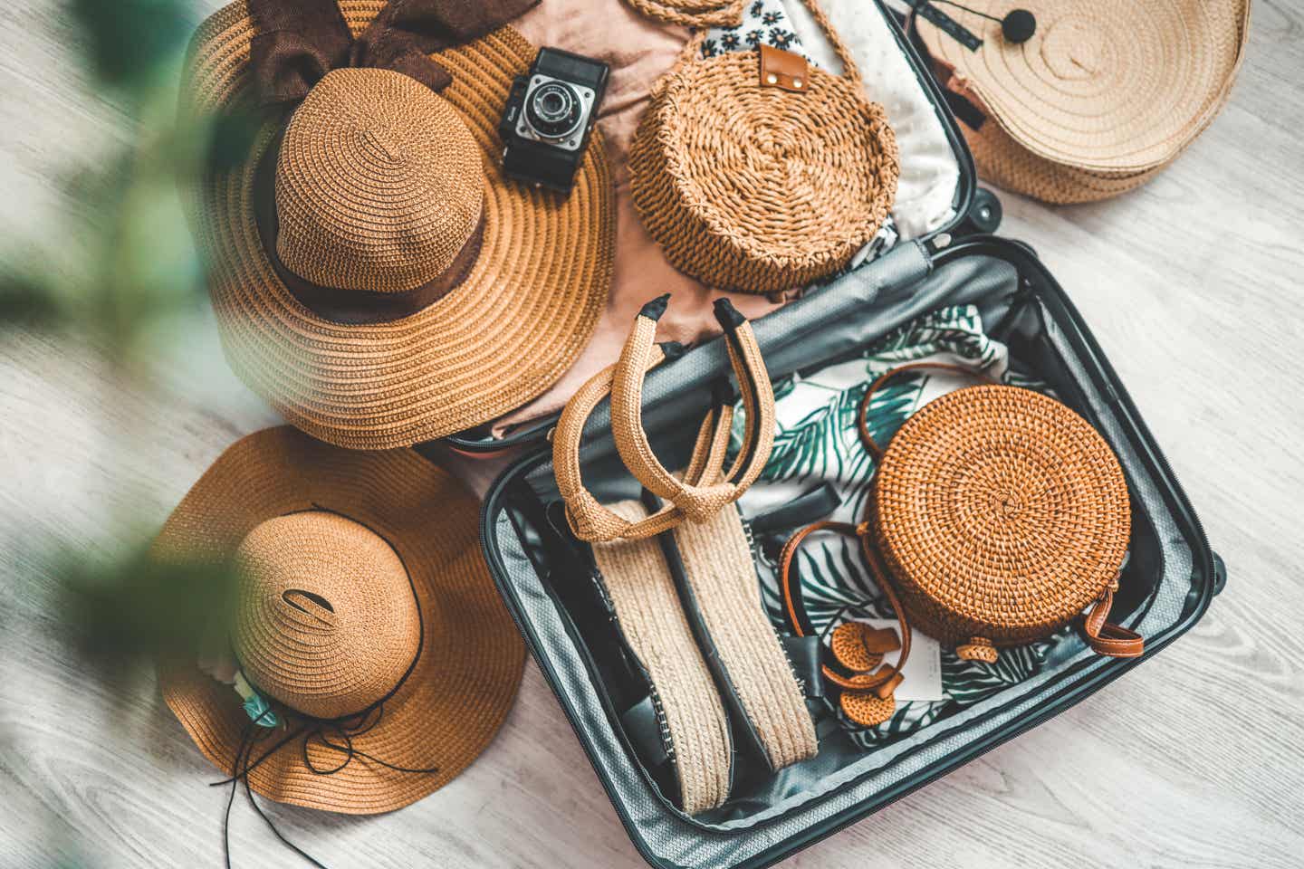 Nachhaltigeres Urlaubs- und Reisekonzept mit Koffer, Strohhut, Basttasche und Accessoires aus Naturmaterialien auf Holzboden