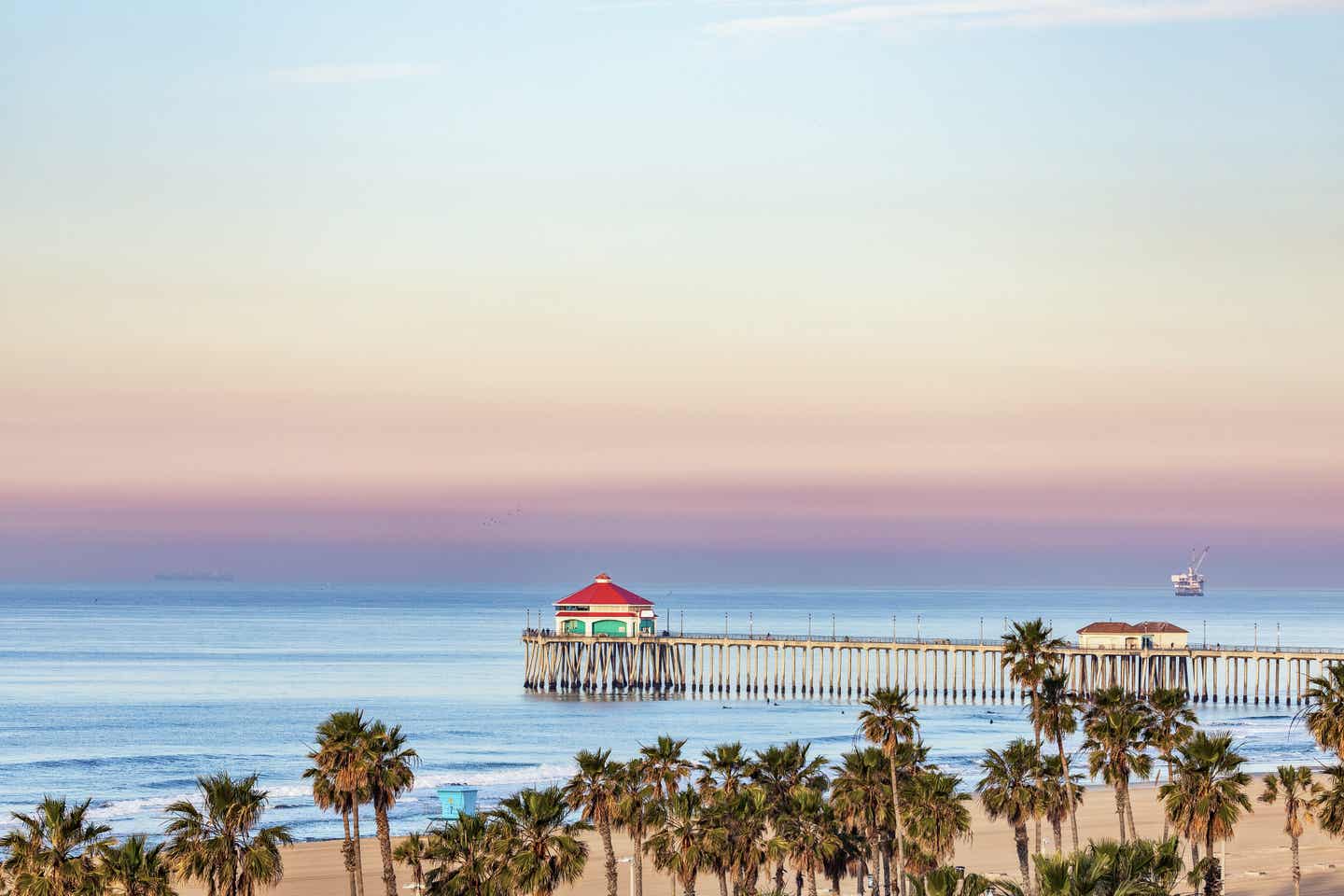 Der Pier des Huntington Beach bei Sonnenaufgang mit Palmen im Vordergrund