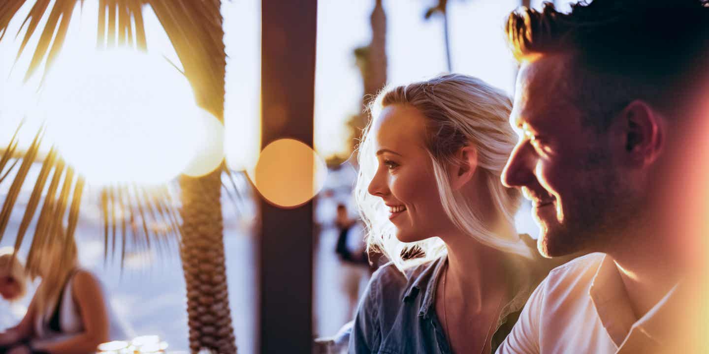 Paar bei Sonnenuntergang in einer Ibiza Sunset Bar mit Palmen, Drinks und Blick aufs Meer