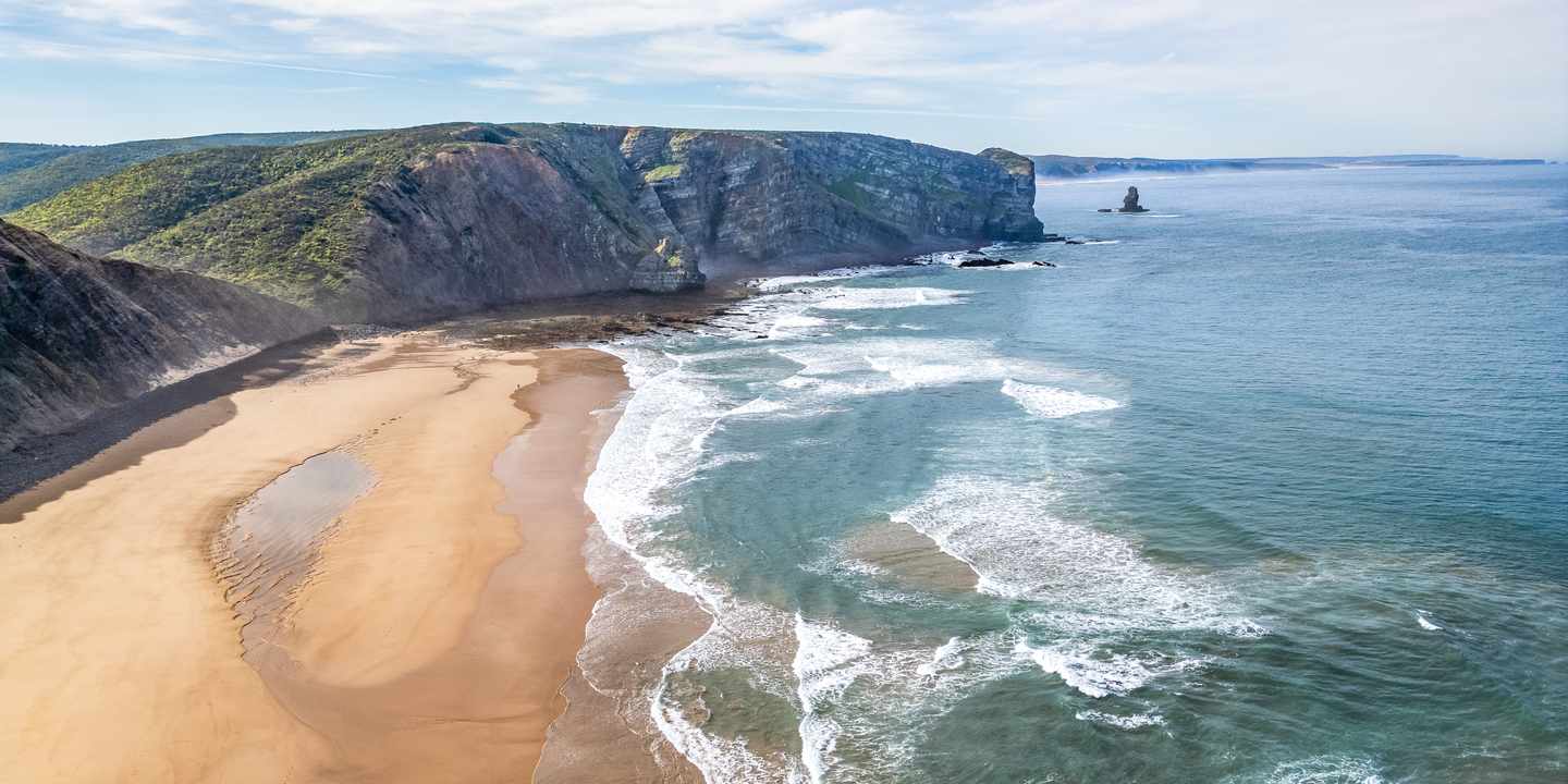 Weitläufiger Naturstrand an Portugals Westküste mit hohen Klippen und Atlantikwellen bei der Algarve