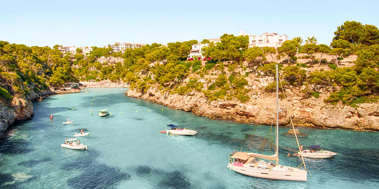 Blick auf eine Bucht auf den Balearen mit glasklarem Wasser und grüner Landschaft im Hintergrund