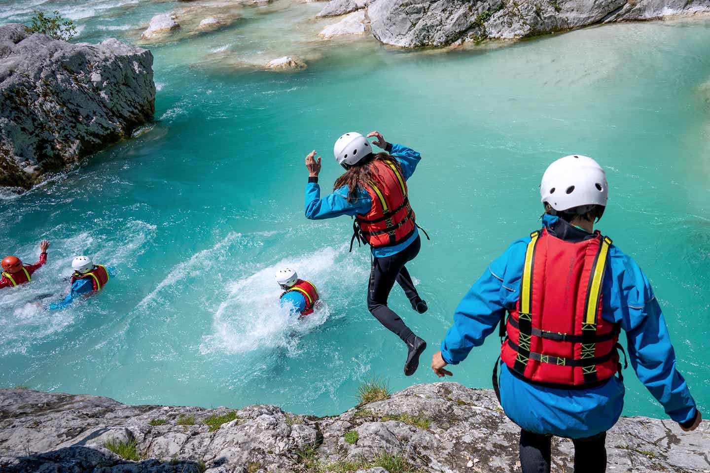 Mensch springt mit Weste beim Canyoning von einem Fels ins Wasser