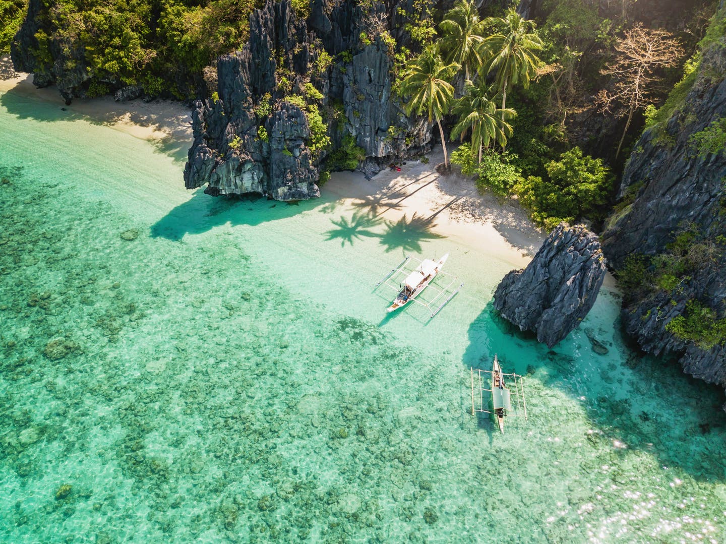 Reisemagazin – Strand vor Palmen und Felsen, türkisblaues Wasser, Boote