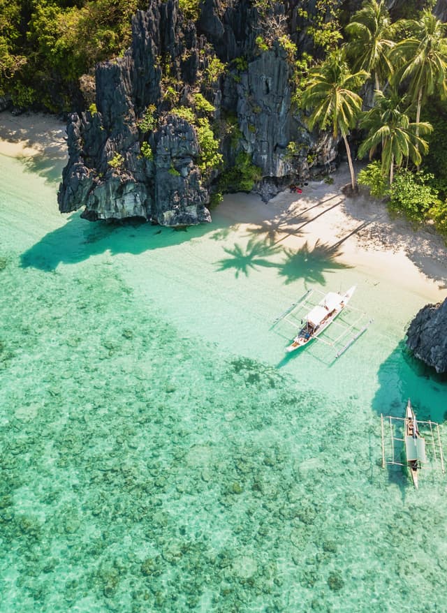 Top-Themen Reisemagazin – Strand vor Palmen und Felsen, türkisblaues Wasser, Boote