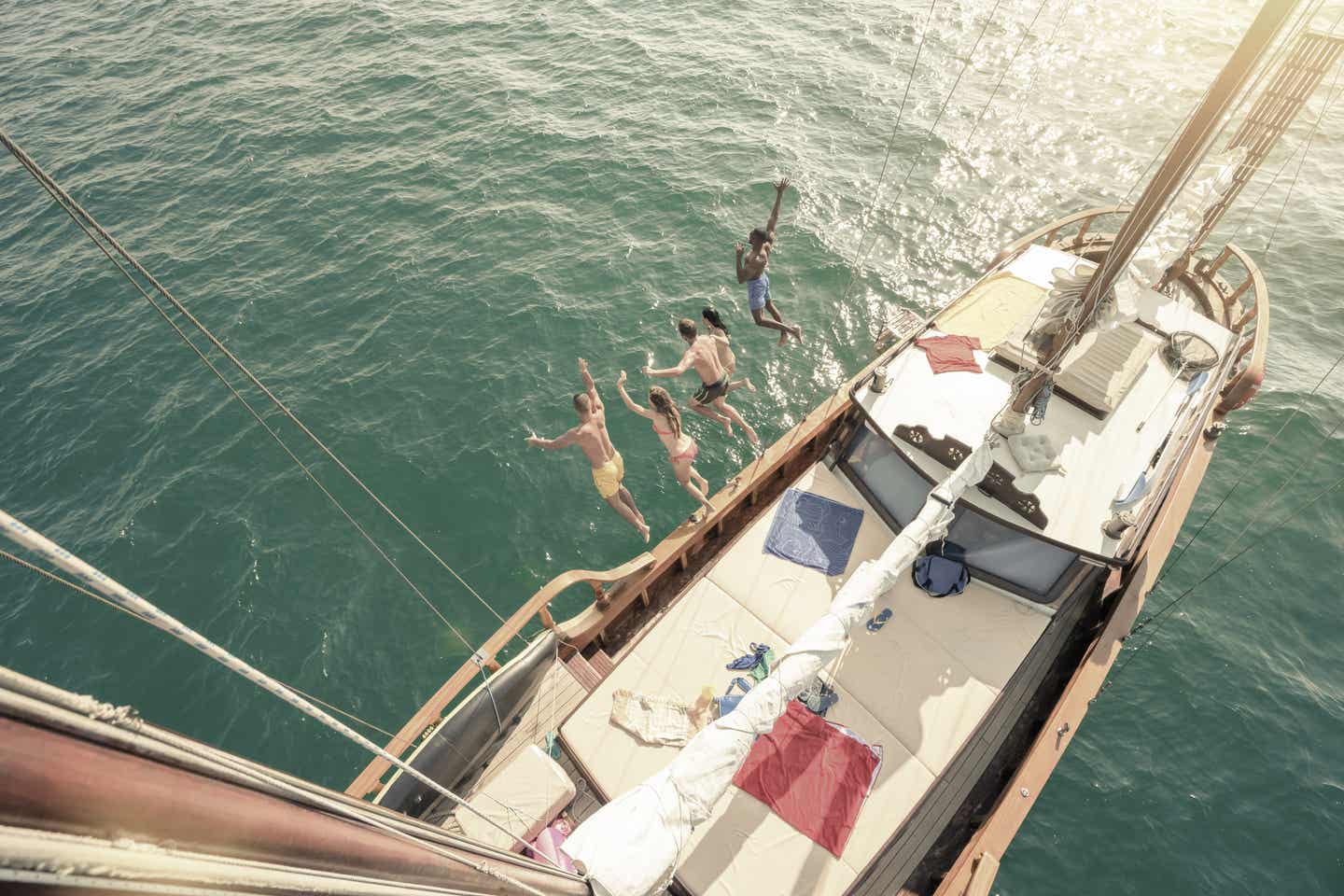 Ibiza Urlaub mit DERTOUR. Eine Gruppe junger Menschen springt von einem Segelboot ins Mittelmeer