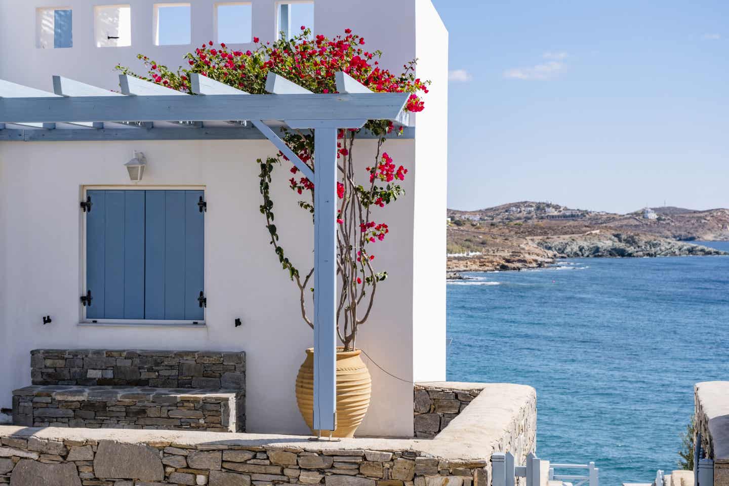Weißes Cottage mit blauen Fenstern, Meer im Hintergrund auf einer Griechischen Insel Weißes Cottage mit blauen Fenstern, Meer im Hintergrund auf einer Griechischen Insel