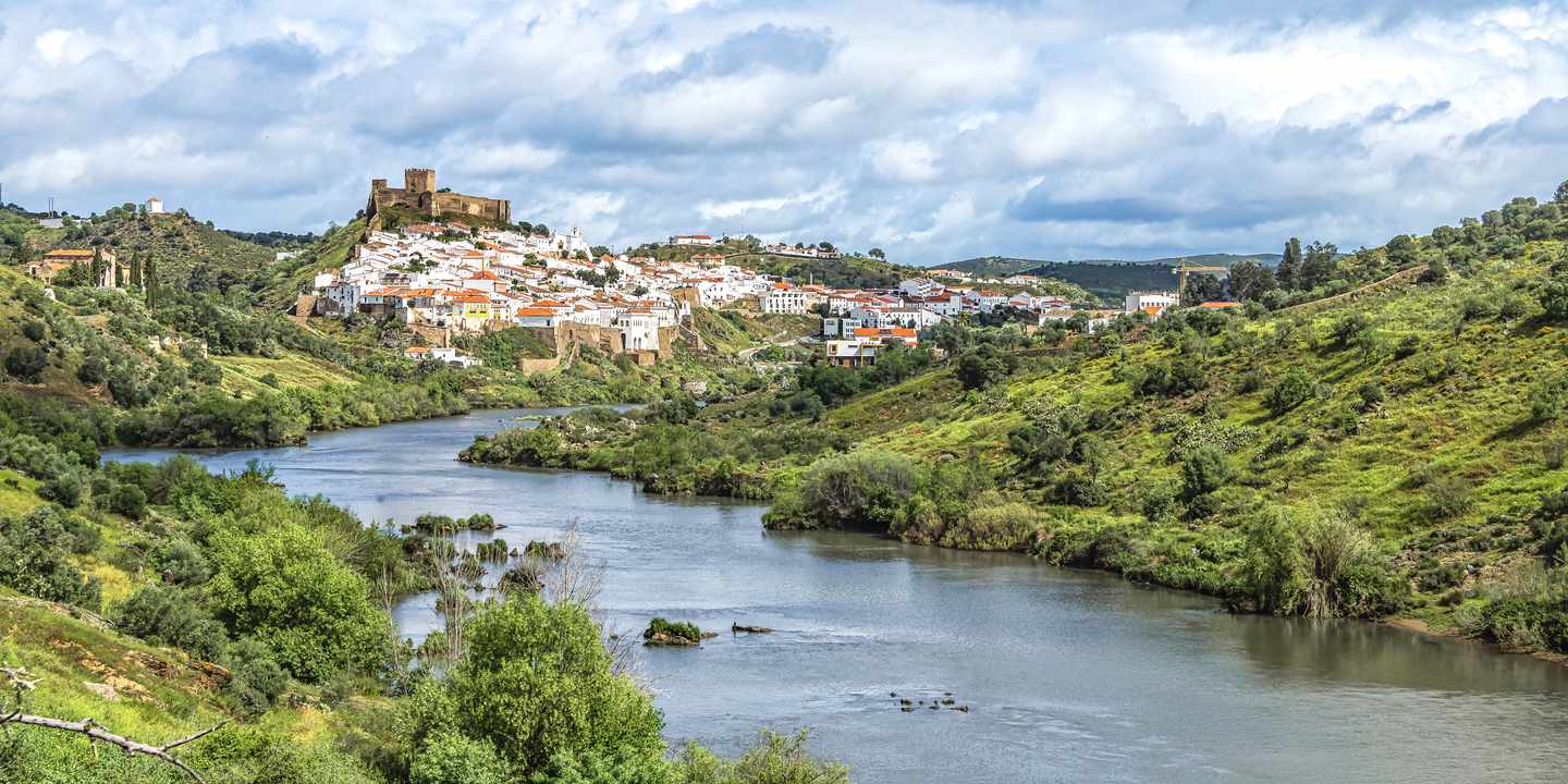 Blick auf den Fluss Guadiana und das weiße Dorf Mértola im Alentejo mit Burganlage auf einem Hügel