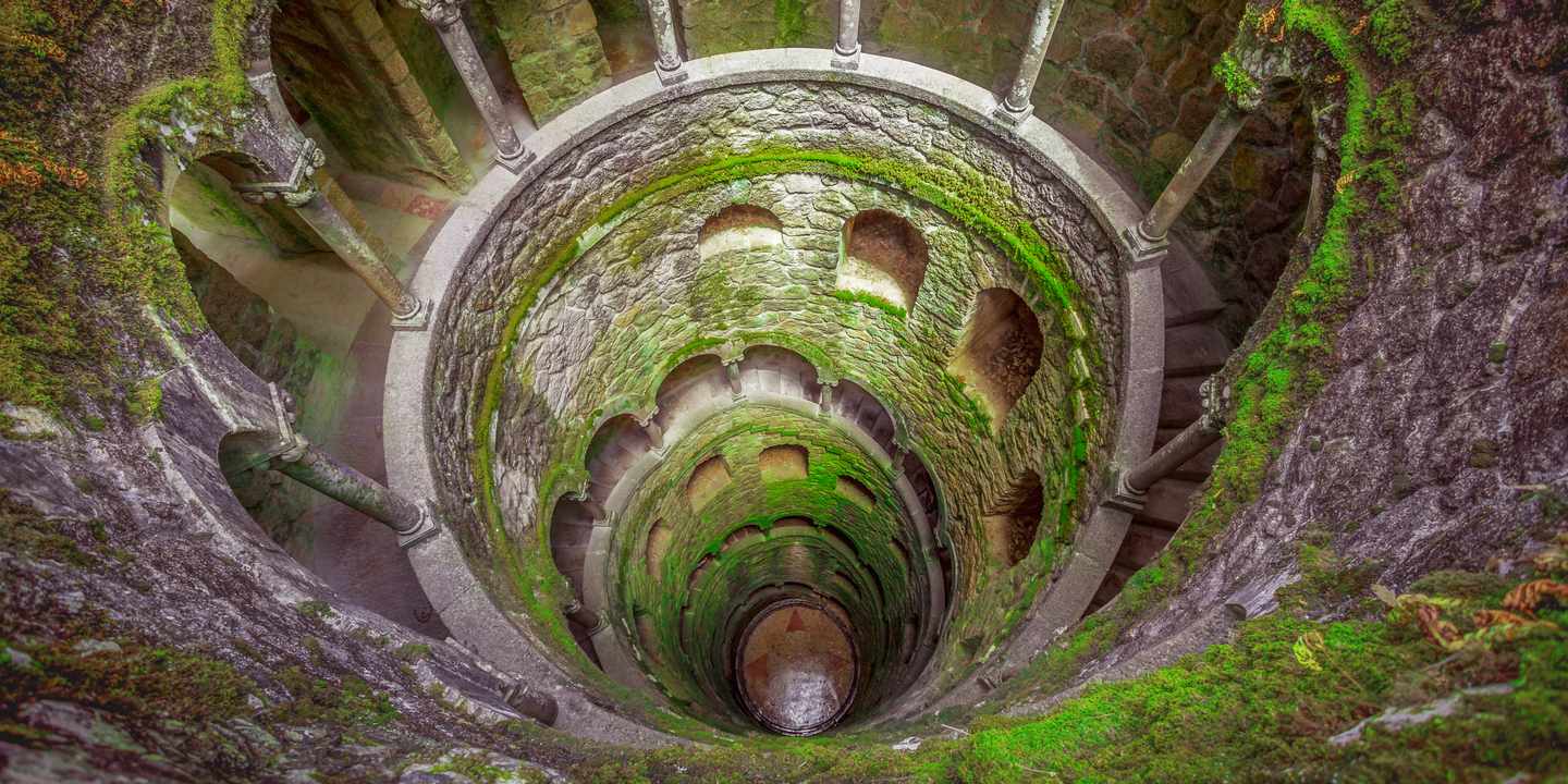 Initiationsbrunnen der Quinta da Regaleira in Sintra mit spiralförmiger Treppe und moosbewachsenen Bögen