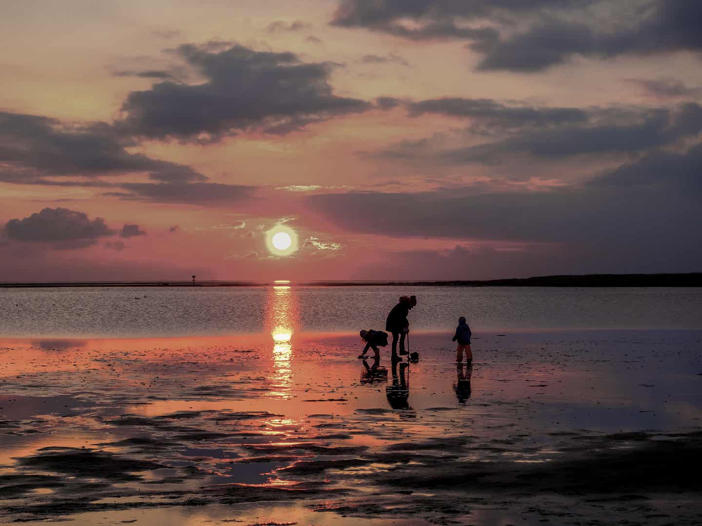 Schleswig Holstein Urlaub mit DERTOUR. Mutter spielt mit zwei Kindern im Wattenmeer bei Sonnenuntergang