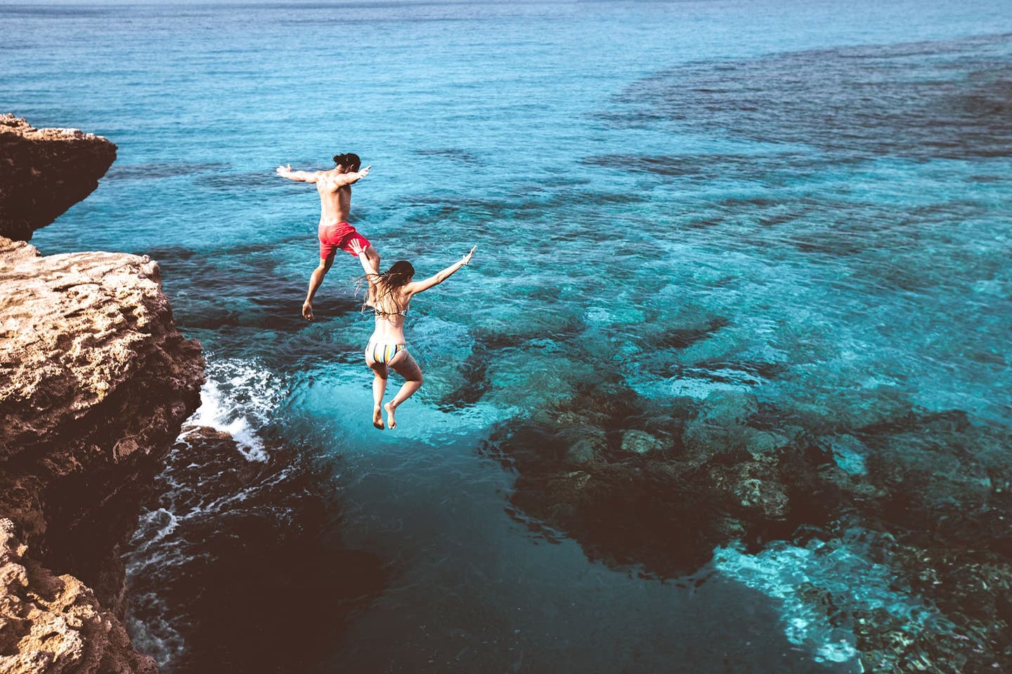 Junges Paar springt von einer Klippe ins Meer