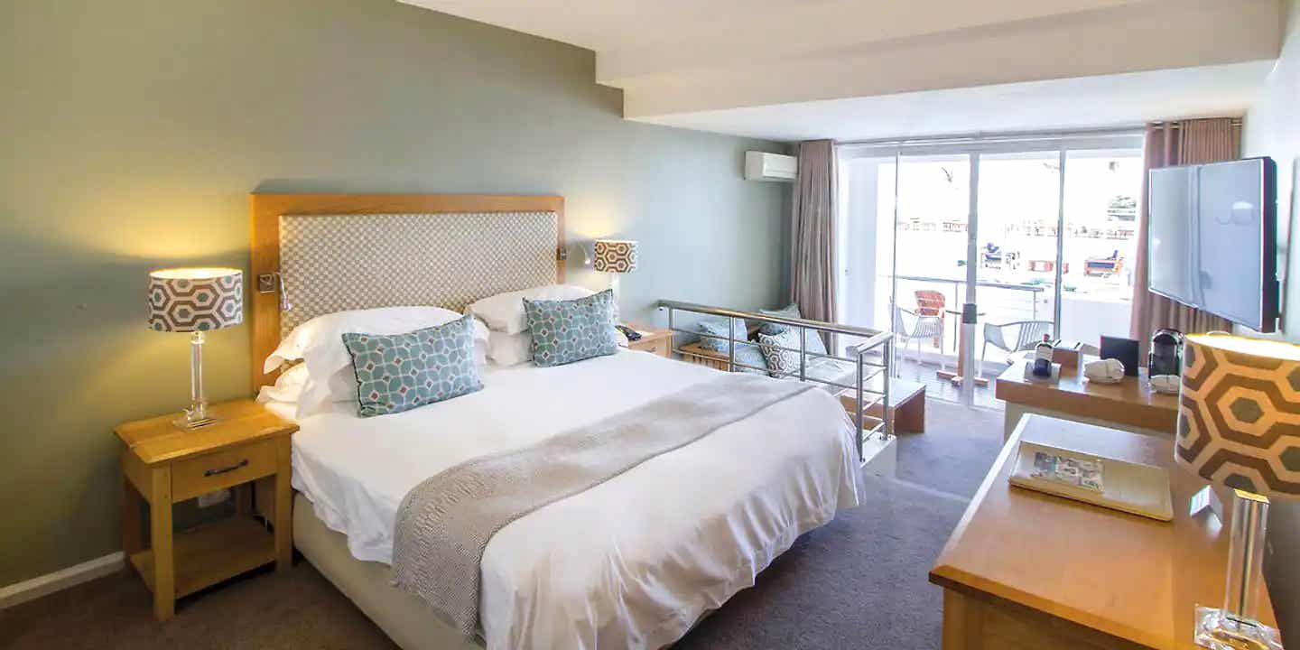 Komfort mit Aussicht – stilvolles Zimmer im The Bay Hotel Kapstadt Modernes Zimmer im The Bay Hotel Kapstadt mit Balkon, Doppelbett, stilvollen Lampen und Blick auf die Poolterrasse