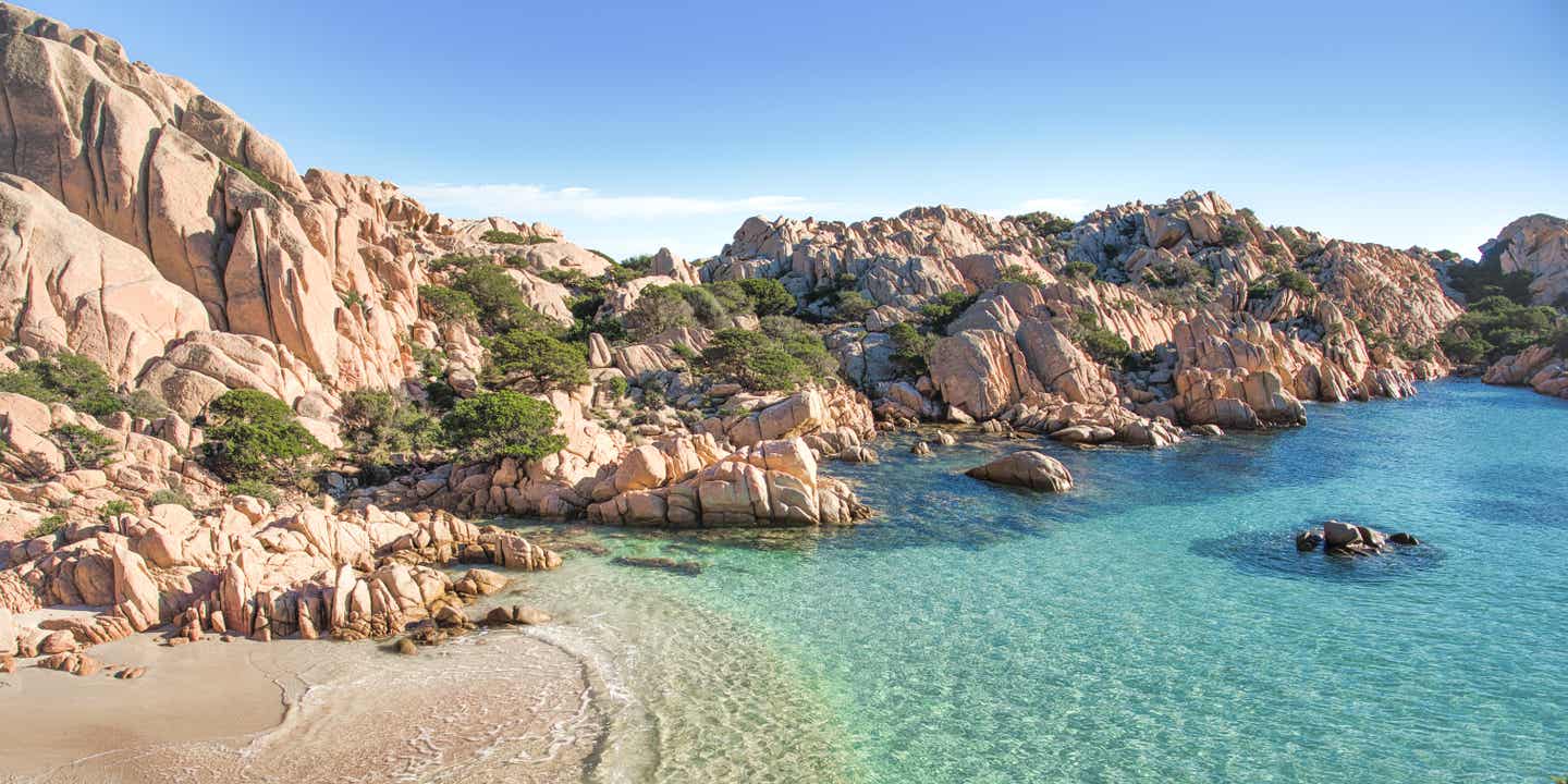 Von schroffen Klippen umrahmter Sandstrand mit türkisblauem Wasser